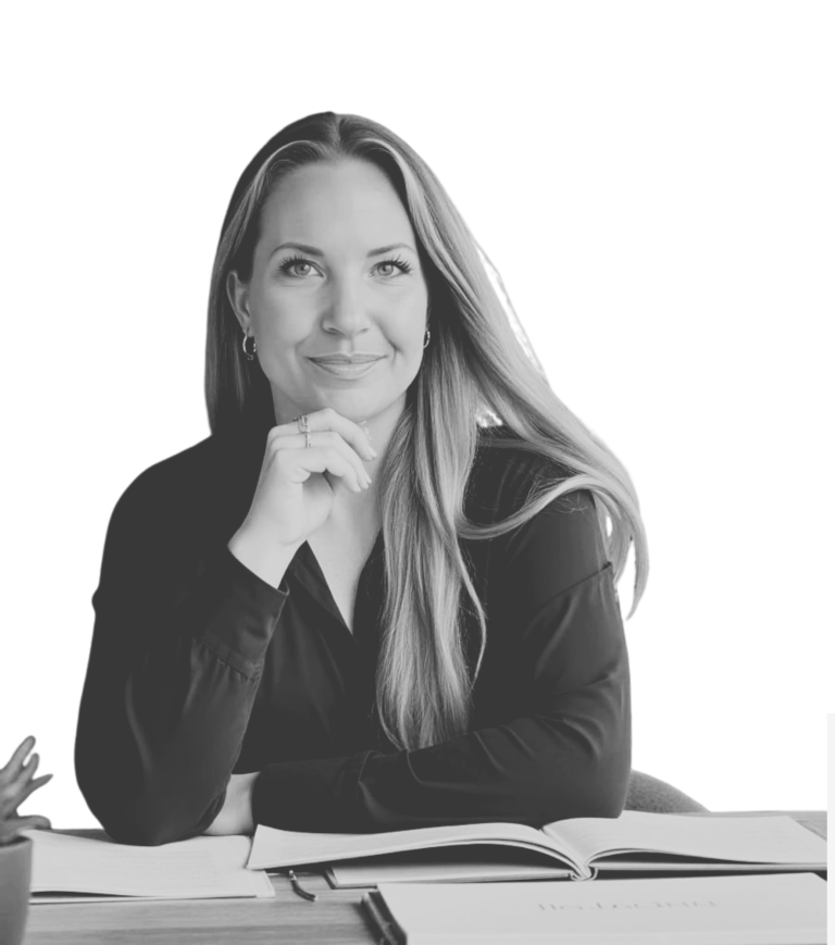 Ein Foto von Daniela Blöcker am Schreibtisch sitzend. Vor ihr Bücher aufgeschlagen auf dem Tisch. Sie schaut selbstbewusst in die Kamera.